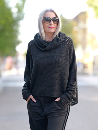 Frau trägt Rundholz Pulli 3420702 schwarz, Grobstrick mit Schalkragen, kombiniert mit Sonnenbrille. Perfekt für Street-Fashion, akzentuiert durch sichtbare Details des Pullovers.