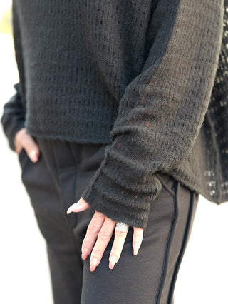 Rundholz Pulli 3420702 schwarz: Eine Person trägt einen grob gestrickten Pullover mit Schalkragen. Der Pullover hat eine lockere Passform und ist aus einer Mischung verschiedener Materialien.