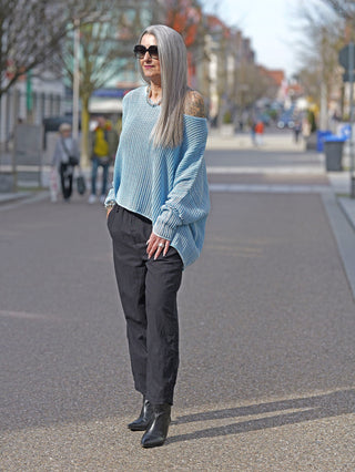 Frau auf Gehweg trägt den Rundholz Strick 3450701 malibu cloud, einen oversized, luftigen Pullover mit sportlichem Netzdesign. Hände in Taschen, schwarze Hose, Sonnenbrille betonen den lässigen Street-Fashion-Look.