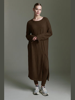 Frau trägt das Cotton Candy Odith Dress espresso, ein langes, locker geschnittenes Strickkleid mit Seitenschlitz und langen Ärmeln, kombiniert mit passenden braunen Leggings und weißen Sneakers.
