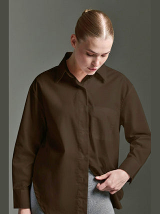 Modell trägt die Cotton Candy Bluse Olivia espresso mit langen Ärmeln und Knopfleiste hinten, kombiniert mit einem hellgrauen Unterteil, während es den Saum der Bluse hält.