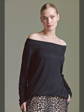 Model trägt das Cotton Candy Ondra Tee black mit Off-Shoulder-Ausschnitt und langen Ärmeln, kombiniert mit einer leopardengemusterten Hose. Die Hand lässig in der Tasche, wirkt der Look elegant und entspannt.