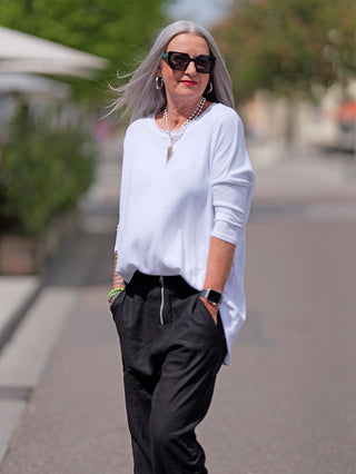 Eine Frau trägt das OFF#DLY Shirt Elli weiß mit lässigem Oversized-Look, Rundhalsausschnitt und 3/4-Ärmeln, kombiniert mit einer Halskette und schwarzen Hosen.