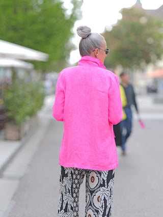 Emily Damenblazer neon pink, getragen von einer Frau. Der Blazer hat Krempelärmel und aufgesetzte Patten, besteht aus gewaschener Leinenqualität und ist einreihig sowie ungefüttert.