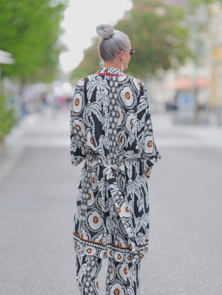 Emily Kimono pink/black/sand, getragen von einer Frau mit Sonnenbrille, lässig gebunden mit Gürtel, zeigt einen Ethno-Print auf fließender Viskose, ideal für Street Fashion.