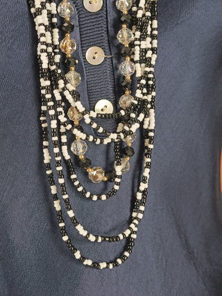 Die OFF#DLY Kette Mya black&white liegt auf einem Hemd, zeigt feine Details wie Kristalle und Perlen, die ihren eleganten Charakter als modisches Accessoire unterstreichen.