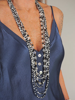 Frau trägt die OFF#DLY Kette Mya black&white, ein modisches Accessoire mit schwarzen und weißen Perlen. Sie kombiniert die Kette mit einem blauen Oberteil, was den stilvollen Look unterstreicht.