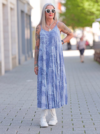 Eine Frau trägt das OFF#DLY Viskose Dress Lydia blue mit schmalen Trägern, kombiniert mit weißen Stiefeln und Sonnenbrille, ein leichtes Sommerkleid aus fließender Viskose.