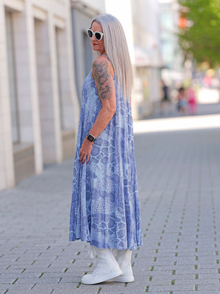 Eine Frau trägt das OFF#DLY Viskosekleid Lydia in Blau, kombiniert mit weißen Stiefeln und Sonnenbrille. Das Kleid hat schmale Träger und besteht aus fließender Viskose.