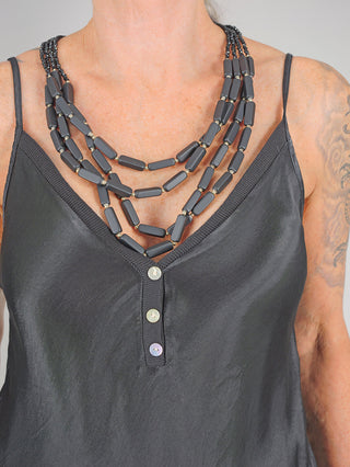 Eine Frau trägt die OFF#DLY Kette Clara black, eine zarte Halskette aus Kunststoff und Glas, etwa 35cm lang, die elegant auf der schwarzen Tanktop-Oberfläche ruht.