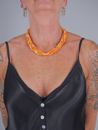 Frau trägt die OFF#DLY Flechtkette orange/gelb, ein modisches Accessoire mit variabler Länge, betont durch ein schwarzes Oberteil.