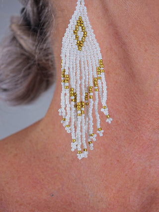 Nahaufnahme eines Ohres mit dem OFF#DLY BoHo Ohrschmuck white/gold, handgefertigte lange Fransenohrringe aus weißen und goldenen Glasperlen. Die Perlen formen ein tropfenförmiges Oberteil mit mehreren herabhängenden Strängen.