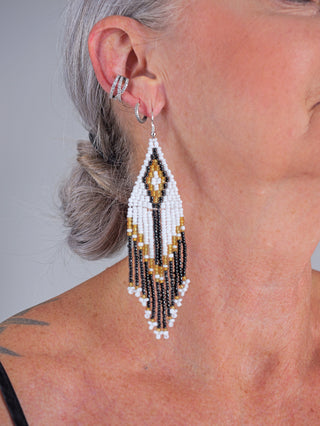 Nahaufnahme einer Frau mit dem OFF#DLY BoHo Ohrschmuck in schwarz/weiß/gold. Der Ohrschmuck ist etwa 11 cm lang und aus Glas gefertigt.