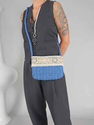 Person trägt die OFF#DLY Crossbag Bast blue, eine blaue und weiße gewebte Tasche mit Reißverschluss. Sie zeigt ein modisches Accessoire über der Schulter, kombiniert mit schwarzer Kleidung.