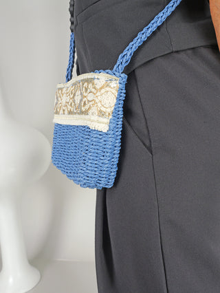 OFF#DLY Crossbag Bast blue, eine bastgeflochtene Umhängetasche mit Zipper, getragen an der Taille einer Frau. Größe 25x18x5 cm, perfekt für modische Akzente.