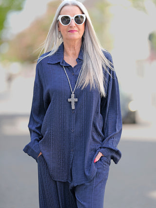 Frau mit langen grauen Haaren trägt die OFF#DLY Summer Shirt Teresa blue, eine langärmelige Longbluse mit Knopfleiste und Kreuzkette, passend für Größe 42/44.
