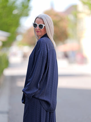 Frau trägt OFF#DLY Summer Shirt Teresa blue, eine lang geschnittene, bequeme Bluse mit Knopfleiste. Sie kombiniert es mit Sonnenbrille und präsentiert einen modernen, lässigen Look.