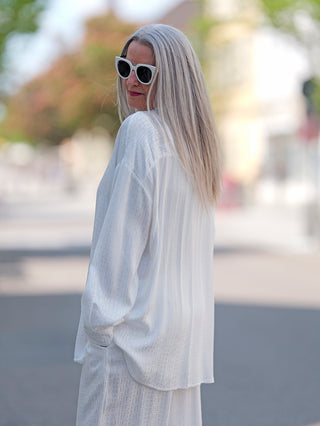 Frau trägt die OFF#DLY Summer Shirt Teresa white, eine lang geschnittene Bluse mit Knopfleiste, ideal für den Sommer. Sie hat lange blonde Haare und weiße Sonnenbrille.