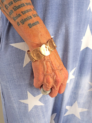 OFF#DLY Armband gold matt, ein breites, mattes Metallarmband am Handgelenk einer tätowierten Person, mit einem auffälligen, schlichten Design, das ideal als modisches Accessoire zur Geltung kommt.
