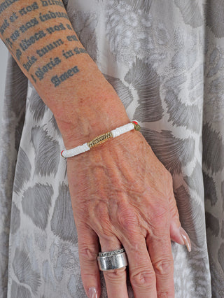 Nahaufnahme des OFF#DLY Armbands in weiß/rot/gold an einem tätowierten Arm, getragen mit einem goldenen Ring, zeigt filigranes Design und metallische Nickelfreiheit.