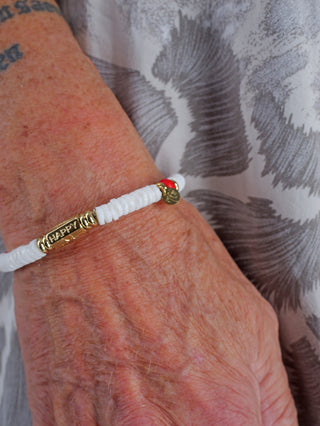 Person trägt das OFF#DLY Armband white/red/gold, ein modisches Accessoire aus nickelfreiem Metall und Tonstein, das als einzigartiger Schmuck am Handgelenk hervortritt.