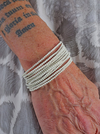 OFF#DLY Monika Armband Set creme, zeigt ein Handgelenk mit mehreren Armbändern aus nickelfreiem Metall und Glas, zusammen mit einem Tattoo auf dem Arm.