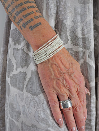 Nahaufnahme eines Arms mit Tätowierung, der das OFF#DLY Monika Armband Set creme trägt, bestehend aus mehreren Armbändern aus nickelfreiem Metall und Glas. Ein Ring ist ebenfalls sichtbar.