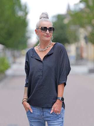 Eine Frau trägt das OFF#DLY Shirt Ursula marine, eine Schlupfbluse mit halber Knopfleiste, kombiniert mit Sonnenbrille und einer Halskette.