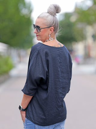 Frau mit Sonnenbrille trägt das OFF#DLY Shirt Ursula marine, eine Schlupfbluse mit halber Knopfleiste aus Leinen und Viskose, während sie über die Schulter zurückblickt.