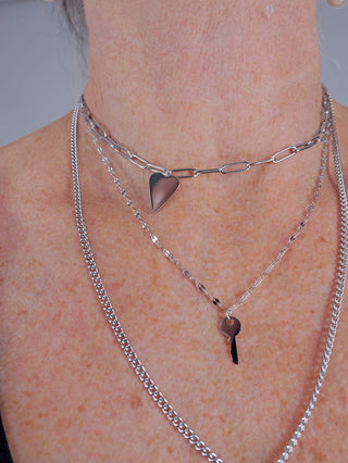 OFF#DLY Kette Ines silber: Eine feine, dreifach geschichtete Halskette mit kleinen Anhängern, einschließlich eines Herzanhängers. Sichtbar getragen von einer Person, Länge etwa 25 cm, nickelfreies Metall.