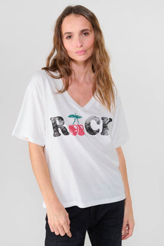 Frau trägt das Indigo Gallery Germany - FAULDI T-Shirt. Lockerer Boyfriend-Schnitt mit V-Ausschnitt und kurzen Ärmeln, aus verwaschenem Stoff, passend zu einem Kirschen-Aufdruck-Rock.