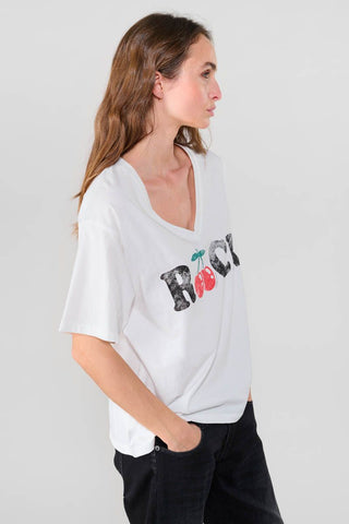 Frau trägt das Indigo Gallery Germany - FAULDI T-Shirt mit V-Ausschnitt und lockerem Schnitt. Das verwaschene Material verleiht einen trendigen Look, passend zu einem Rock mit Kirschen-Aufdruck.