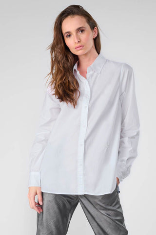 Eine Frau trägt das Shirt Femme Jama mit klassischem Kragen, geradem Schnitt und langen Ärmeln, versehen mit Ton-in-Ton besticktem Monogramm und Knöpfen auf der Rückseite.