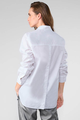 Eine Frau trägt das Shirt Femme Jama mit klassischem Kragen, geradem Schnitt und Knöpfen auf der Rückseite. Das Hemd besticht durch lange Ärmel und ein Ton-in-Ton gesticktes Monogramm.