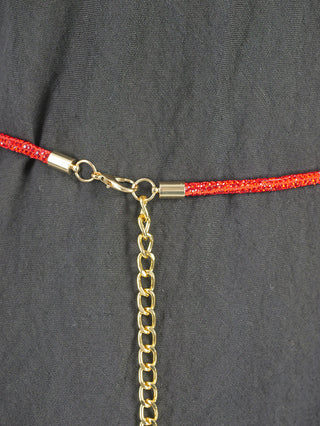 Der OFF#DLY Strassgürtel Bonny red/gold zeigt einen roten, funkelnden Gürtel mit goldenen Metallenden, verbunden durch einen kleinen Karabinerverschluss, von dem eine kurze goldene Kette herabhängt.