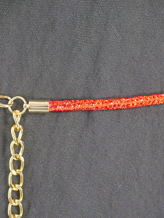 OFF#DLY Strassgürtel Bonny red/gold: Nahaufnahme eines glitzernden roten Kordels mit goldfarbenem Metallabschluss, verbunden mit einer goldenen Kette, auf dunklem Stoff liegend. Ideal als modisches Accessoire.