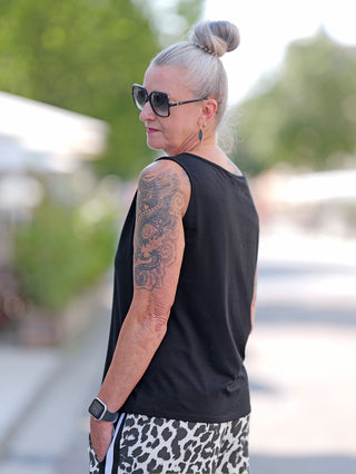 Frau mit Tattoos trägt das Doris Streich Top 561.270 black Chuck mit breiten Trägern und Chuck-Print vorne, kombiniert mit einer Sonnenbrille, im Street-Fashion-Look.