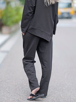 Person trägt OFF#DLY Joggpant Lilly black, schmal geschnitten mit Gummizug und ohne Bündchen unten, aus 100% Baumwolle. Sichtbar mit schwarzen Sandalen, geeignet für Größen bis 40/42.