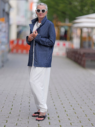 Ältere Frau trägt den OFF#DLY Denim Blazer Ulla, einen leichten Longblazer mit aufgesetzten Taschen, während sie auf einer gepflasterten Fußgängerstraße steht.