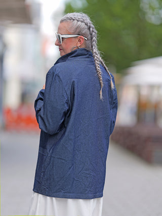 Person trägt den OFF#DLY Denim Blazer Ulla, ein locker sitzender, dunkelblauer Longblazer mit aufgesetzten Taschen, über einem hellen Kleid.