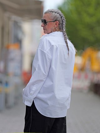 True Religion Bluse Double Cuff Oversized, getragen von einer Frau mit langen geflochtenen Haaren und Sonnenbrille. Die Bluse hat eine Knopfleiste, großen Kragen und Doppelmanschetten.
