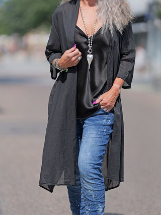 Frau trägt den OFF#DLY Kimono Roxy schwarz, ein leichter, knielanger Baumwollkimono. Sichtbar sind der elegante Schnitt und der fließende Stoff. Perfekt für modische, legere Anlässe.