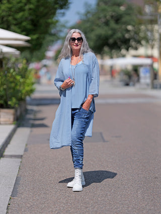 Frau trägt OFF#DLY Kimono Roxy lightblue, einen leichten, langärmeligen Baumwoll-Kimono. Kombiniert mit weißen Stiefeln, im Street-Fashion-Stil. Ideal für legere Anlässe.