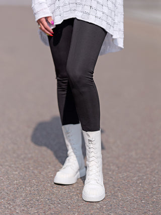 Eine Person trägt die Senoritas ICON Pant Batman in Schwarz; eng anliegende, hochgeschnittene Leggings kombiniert mit weißen Stiefeln.