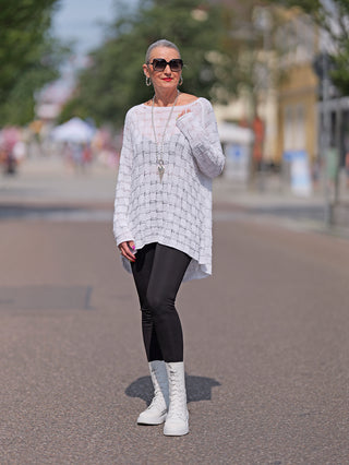 Eine Frau trägt die Senoritas ICON Pant Batman black, eine High Waist Legging aus Viskose-Mix. Kombiniert mit weißem Pullover, Sonnenbrille und weißen Stiefeln, präsentiert sie Street Fashion.