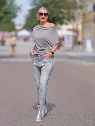 Frau in LTC Girlfriend high waist destroy grey Jeans mit hohem Bund und lockerem Schnitt, kombiniert mit silbernen Stiefeln, auf der Straße spazieren gehend, trägt Sonnenbrille und roten Lippenstift.