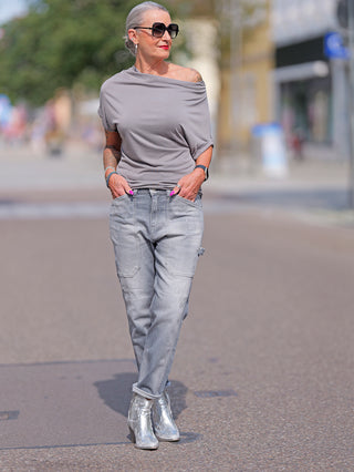 Frau in LTC Girlfriend high waist destroy grey Jeans mit hoher Taille, lockerem Beinschnitt und gestopften Löchern, trägt silberne Stiefel und Sonnenbrille, steht lässig auf der Straße.