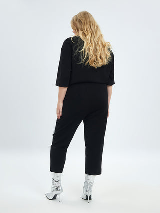 Frau in einem schwarzen MAT Hose 2041 Joggpant mit silberglänzender Applikation und silbernen Schuhen, mit elastischem Bund, ideal für modischen Komfort und stilvolle Freizeitkleidung.