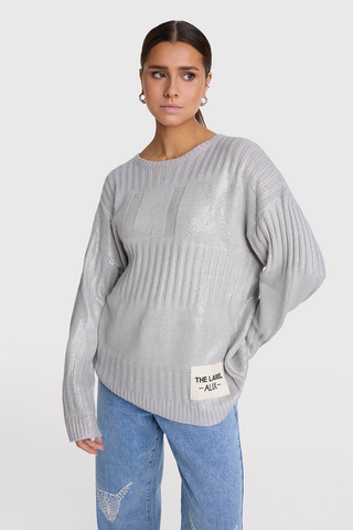 Frau trägt ALIX Foil Pullover champagner mit langem Arm und Rundhalsausschnitt, gestrickt aus weichen Effektgarnen mit Allover-Foliendruck und ALIX-Jacquardmuster. Bequeme Passform, sichtbar über Jeans.