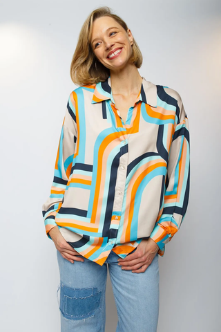 Emily Bluse 791 orange/sand: Frau trägt farbenfrohe Shirtbluse mit Stehkragen, V-Ausschnitt, schmalen Manschetten und modernem geometrischen Print. Hände in den Taschen, lässig und stilvoll.